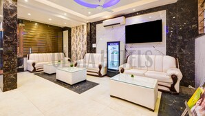A modern living room with two white sofas, glass coffee tables, a ceiling fan, and a flat-screen TV mounted on the wall. - Olivia Hotels @ Delhi Airport (New Delhi)