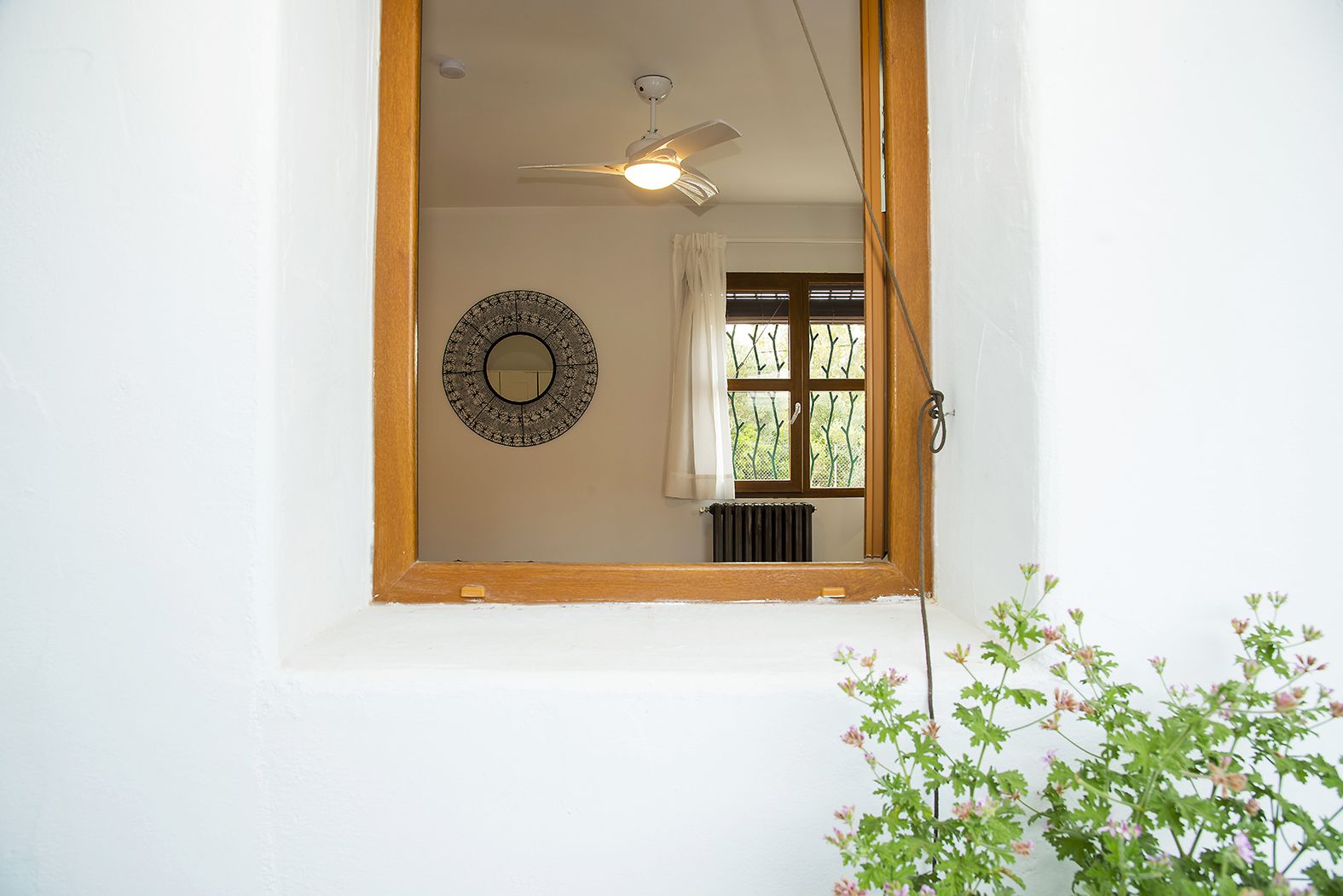 A room with a ceiling fan, a window with curtains, a radiator, and a decorative mirror on the wall.
