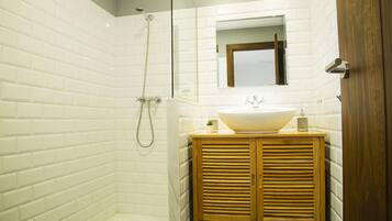 Un baño con azulejos blancos tipo metro, un tocador de madera, un lavabo grande, un espejo y una ducha con cabezal de ducha manual.