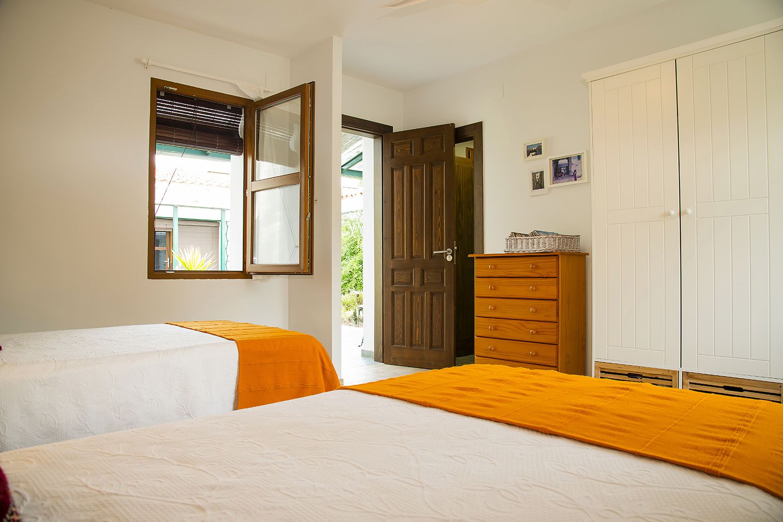 A bedroom with two beds, a wooden dresser, a wardrobe, and a window with blinds.