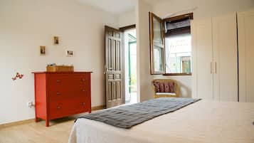 A bedroom with a bed, a red dresser, a wicker chair, and a wardrobe.
