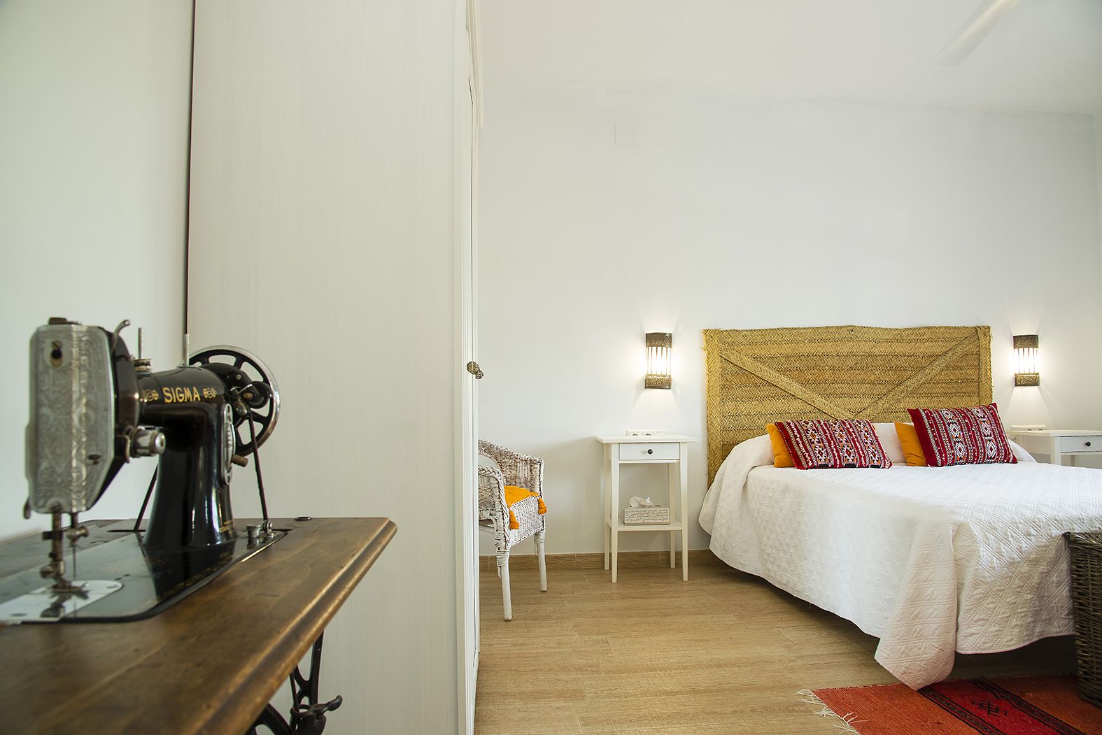 A bedroom with a bed, a sewing machine, a nightstand, and a chair.