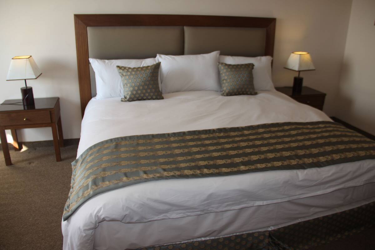 Una cama bien hecha con una colcha estampada, dos mesitas de noche con lámparas y un cabecero de madera.