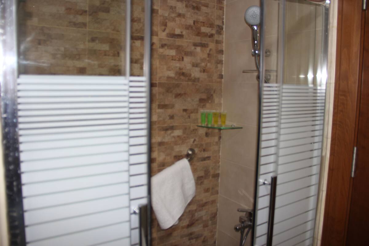 Un baño con cabina de ducha de vidrio, una toalla colgada en un perchero y un estante con artículos de aseo.
