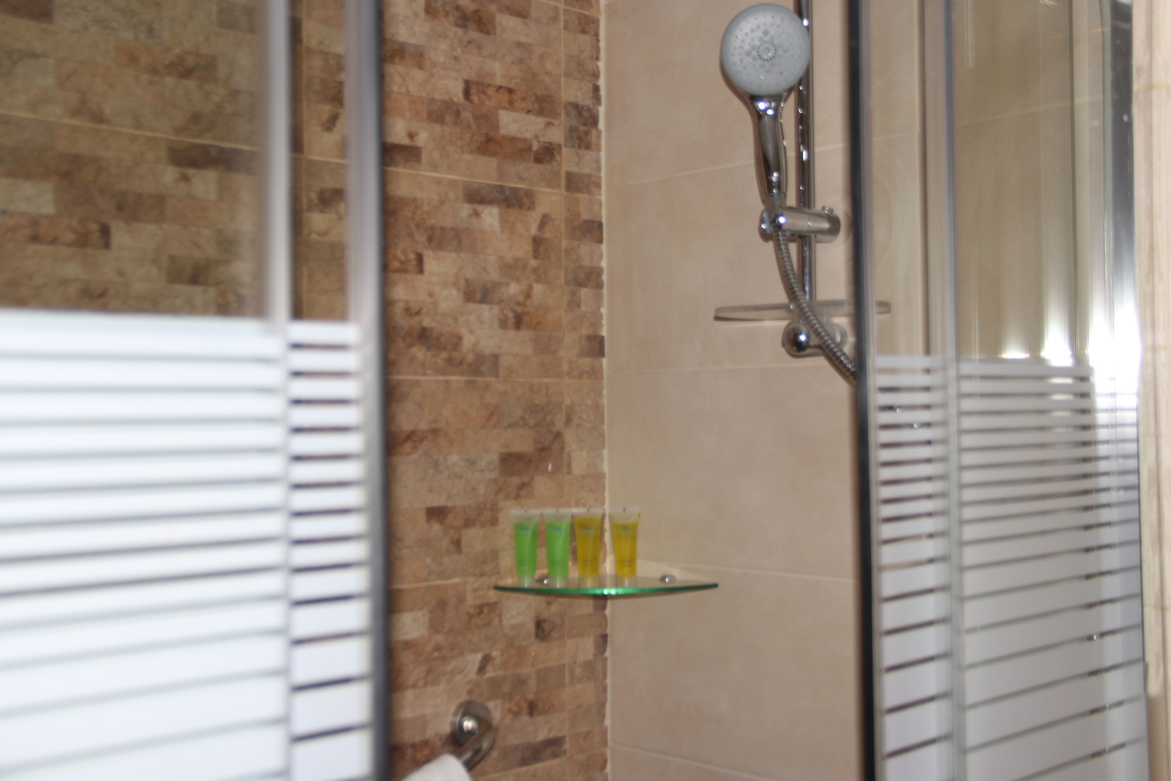 Un baño con ducha, un estante de vidrio con artículos de aseo y pared de azulejos.