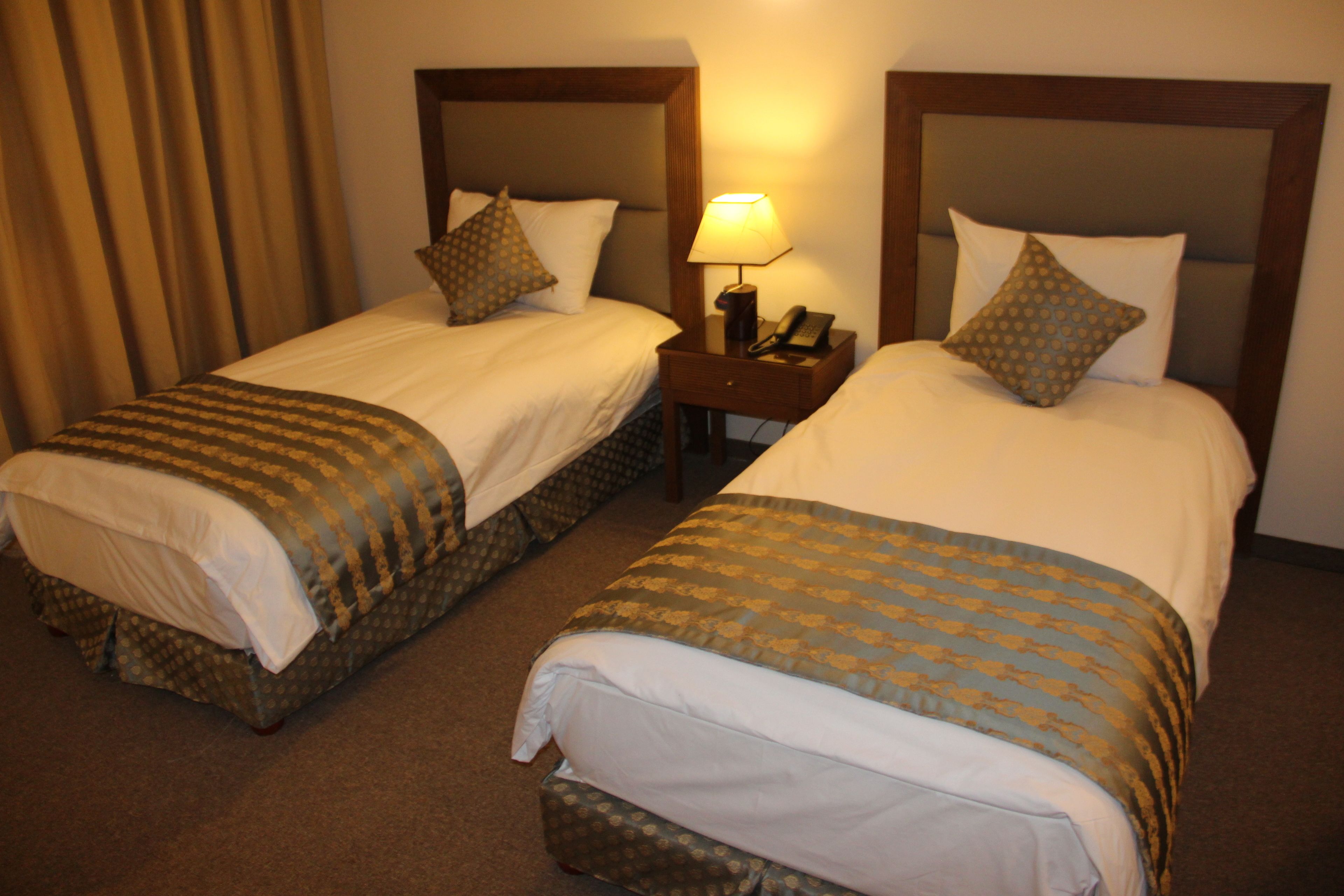 Two adjacent hotel beds with headboards, a nightstand with a lamp, and a telephone.
