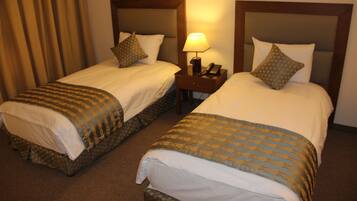 Two adjacent hotel beds with headboards, a nightstand with a lamp, and a telephone.