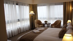 A hotel room with a large bed, two chairs, a small table, and a lamp. - Saray Hotel (Amman)