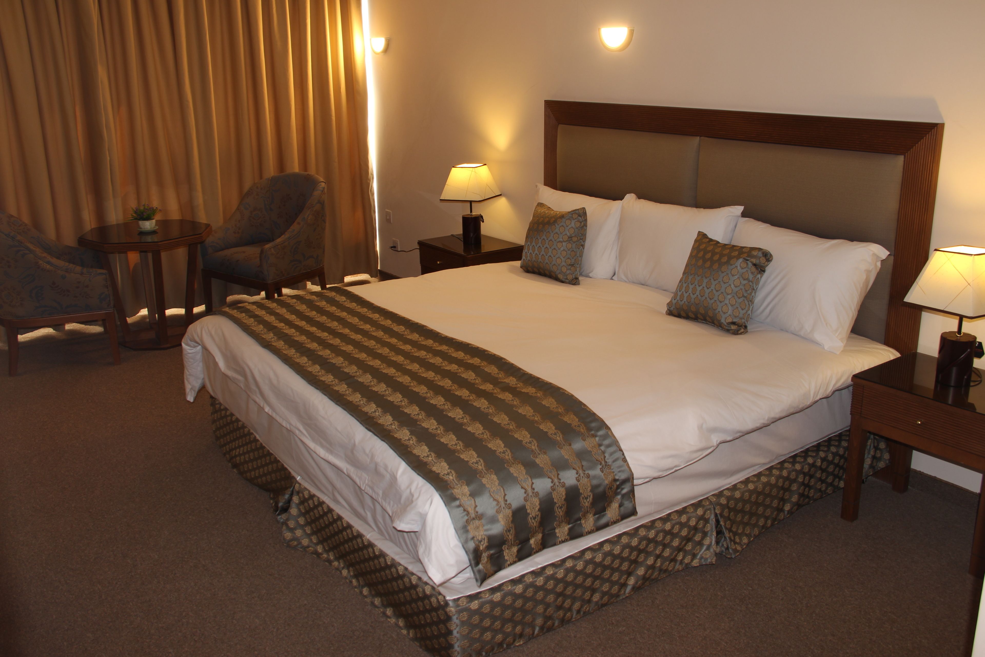 A hotel room with a large bed, two bedside tables with lamps, a chair, and a small table with a plant.