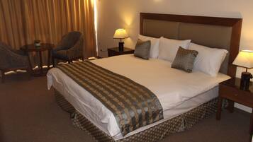 A hotel room with a large bed, two bedside tables with lamps, a chair, and a small table with a plant.