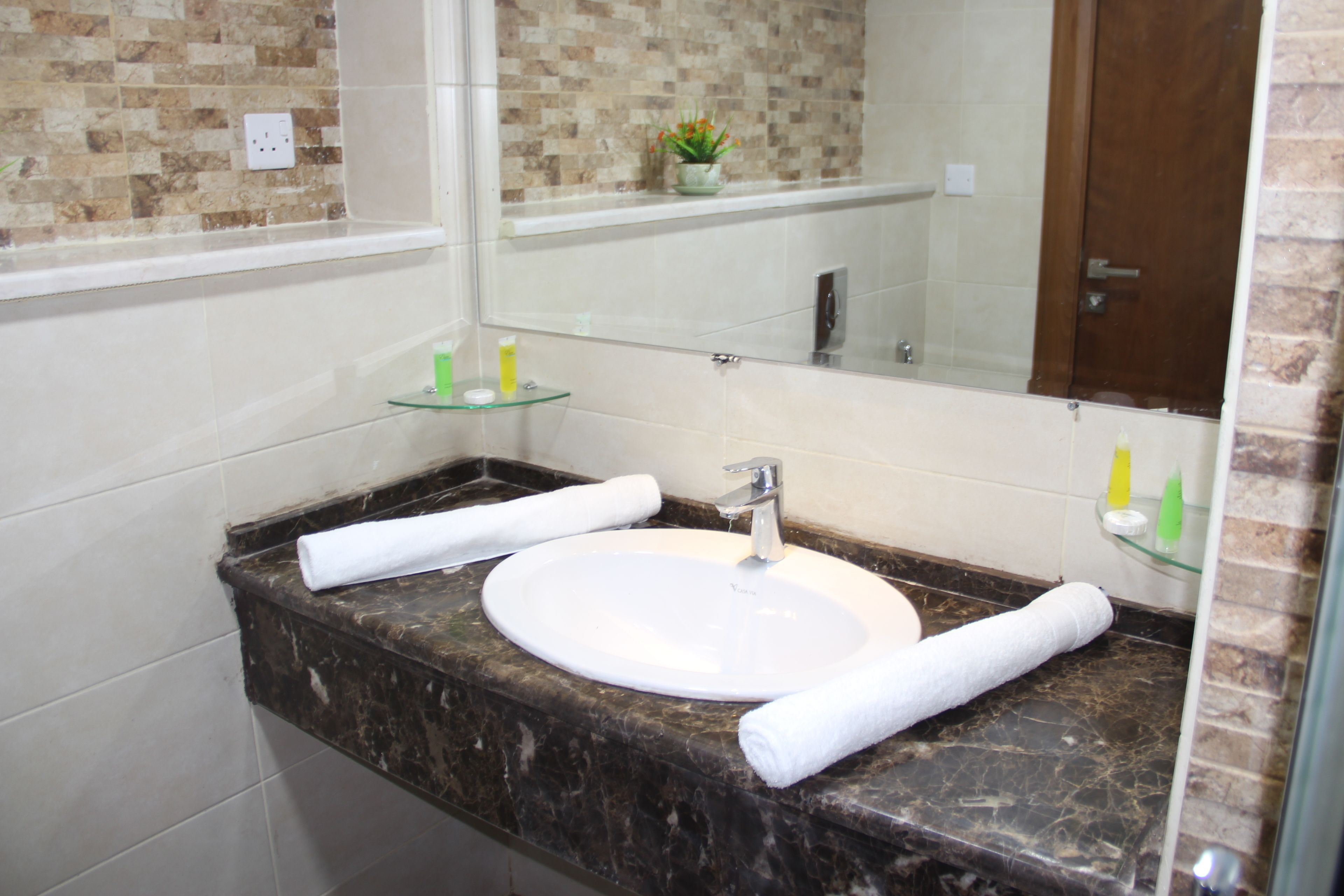 A bathroom with a white sink, marble countertop, and a glass shelf with toiletries.