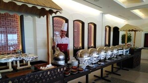 A buffet setup with multiple serving stations, a chef, and decorative elements like patterned screens and a wooden canopy. - Saray Hotel (Amman)