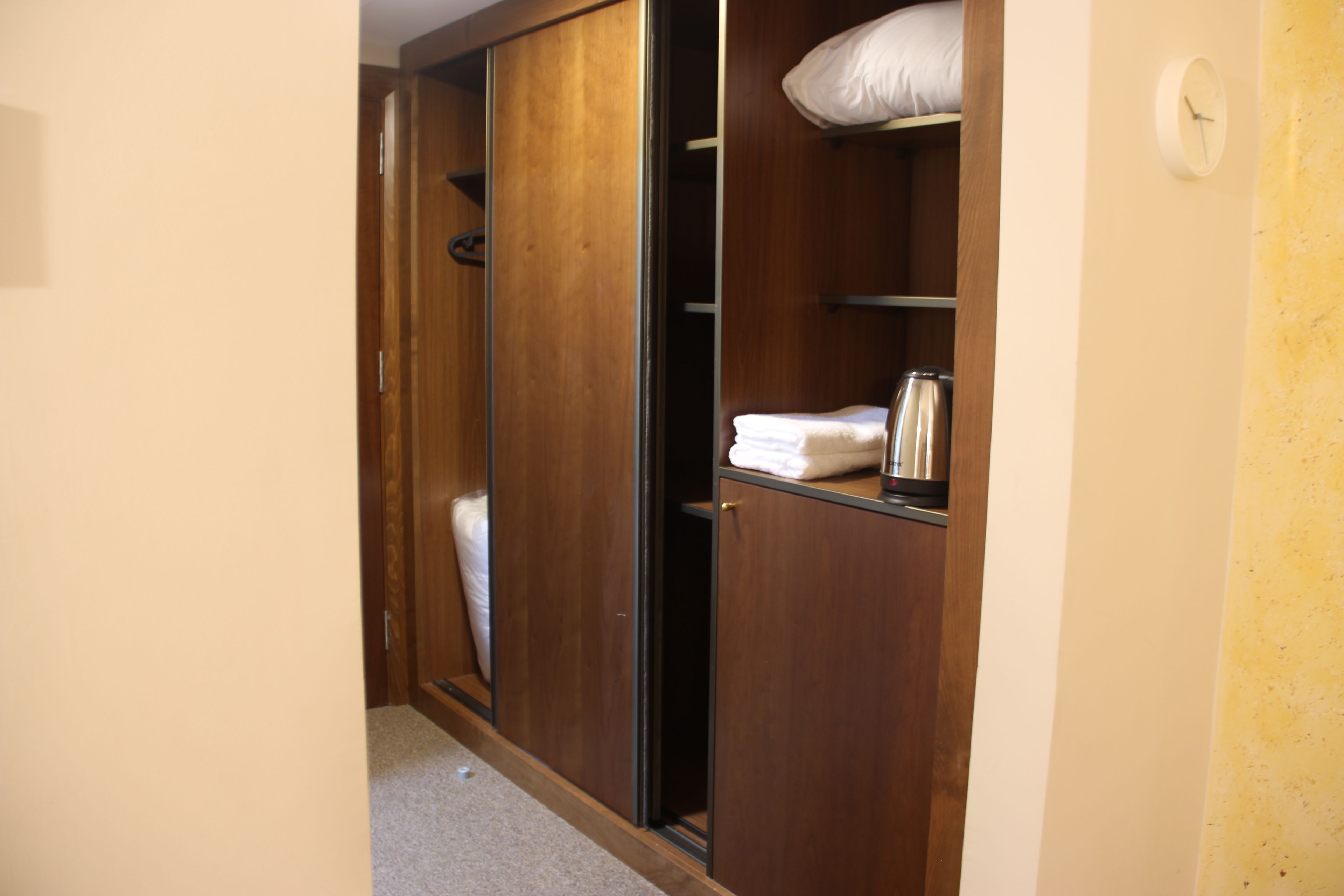 A walk-in closet with wooden doors, a shelf with folded towels, and a white pillow on the shelf.