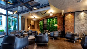 Un hall d’hôtel moderne avec des canapés en cuir, un mur végétal et un mur en briques apparentes.