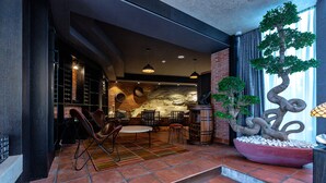 Un intérieur moderne avec un mur en pierre, un grand bonsaï et un espace détente comprenant des chaises et une table.