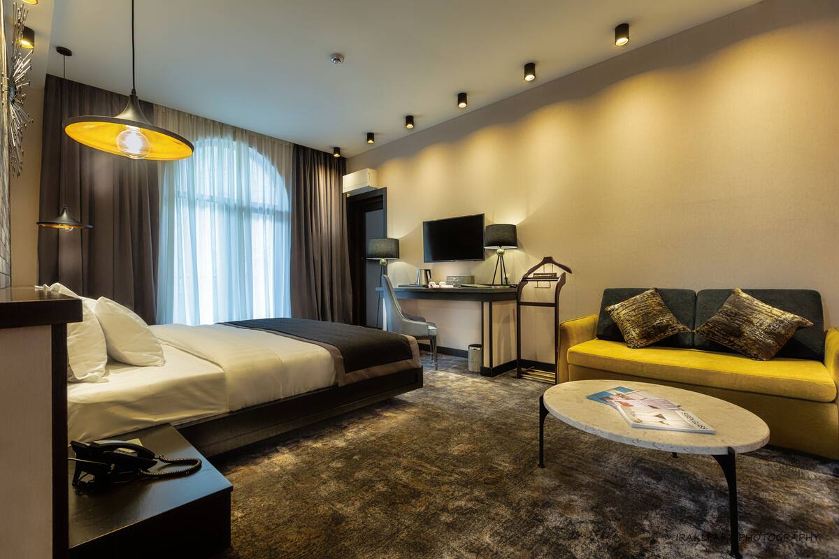 A modern hotel room with a bed, a sofa, a desk, and a television.