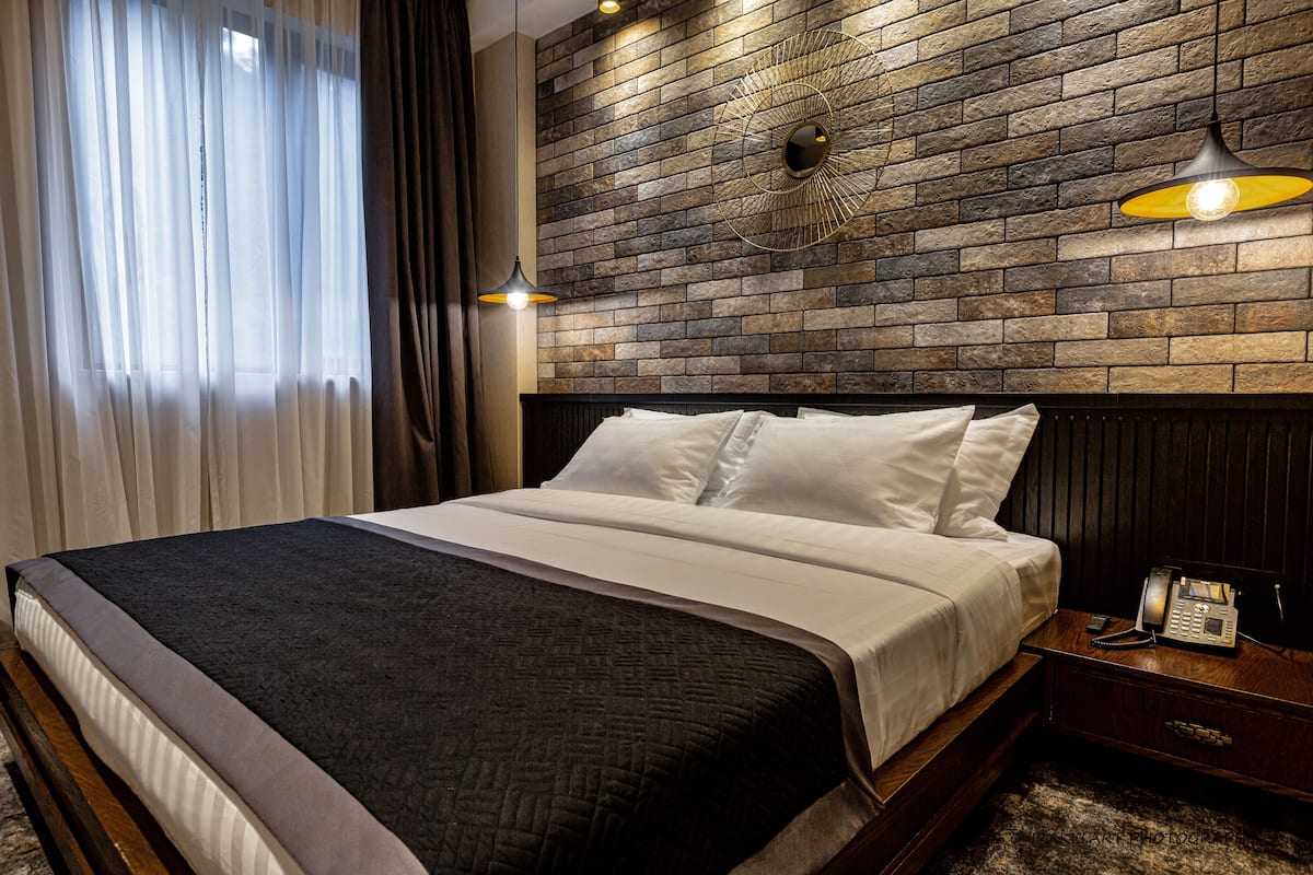 A neatly made bed with white linens, a dark headboard, and a wooden nightstand with a telephone.