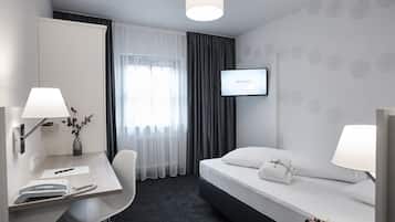 Quarto de hotel com escrivaninha, cadeira, cama e televisão exibindo 'DZ BANK'.