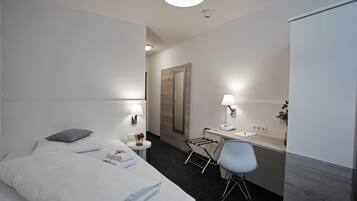 Una habitación de hotel moderna con una cama bien hecha, un escritorio con silla, una mesita con lámpara y un espejo en la pared.