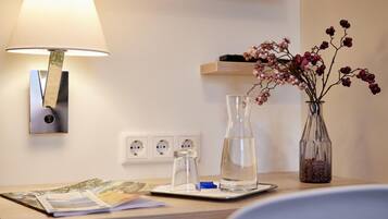 A neatly arranged desk with a lamp, a vase with flowers, a water bottle, and a glass jar.