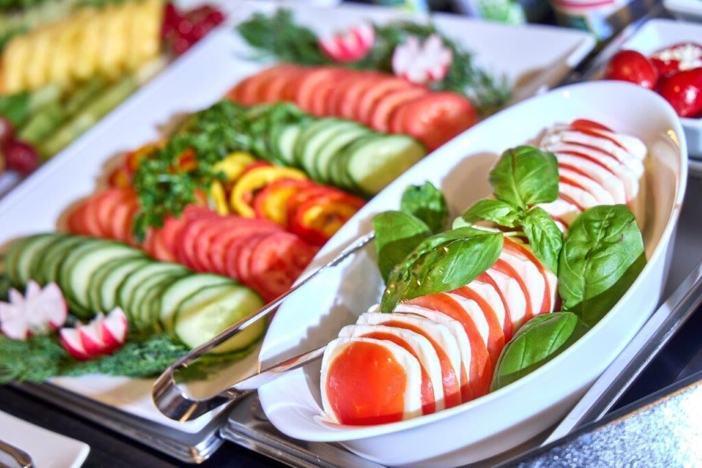 A buffet with various sliced vegetables and fruits, including cucumbers, tomatoes, and radishes, arranged on a white plate.