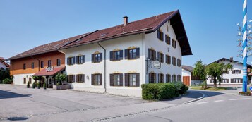 A two-story hotel with a red-tiled roof, multiple windows with shutters, and a sign indicating it is a hotel.