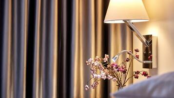 A modern lamp with a curved arm and a frosted lampshade, positioned next to a wall-mounted light switch and a vase with dried flowers.