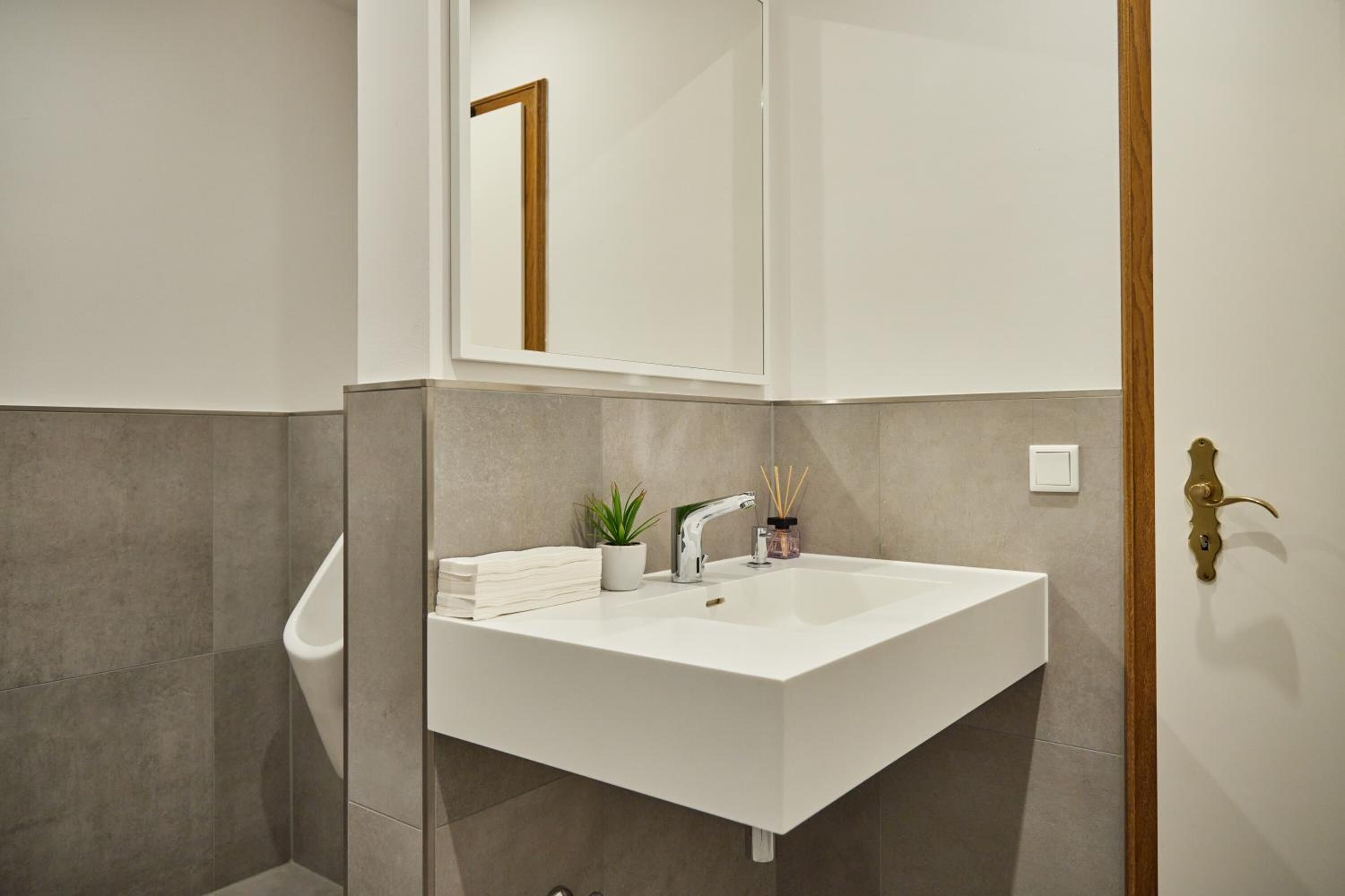 Un baño moderno con un tocador blanco, un espejo y una pequeña planta en maceta.