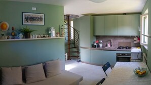 Un espacio habitable compacto con kitchenette, sofá, escalera y comedor.