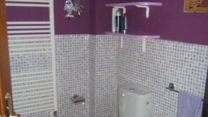 Un baño con inodoro, bidé y lavamanos. Las paredes son moradas, el suelo está cubierto de azulejos y hay un tragaluz.