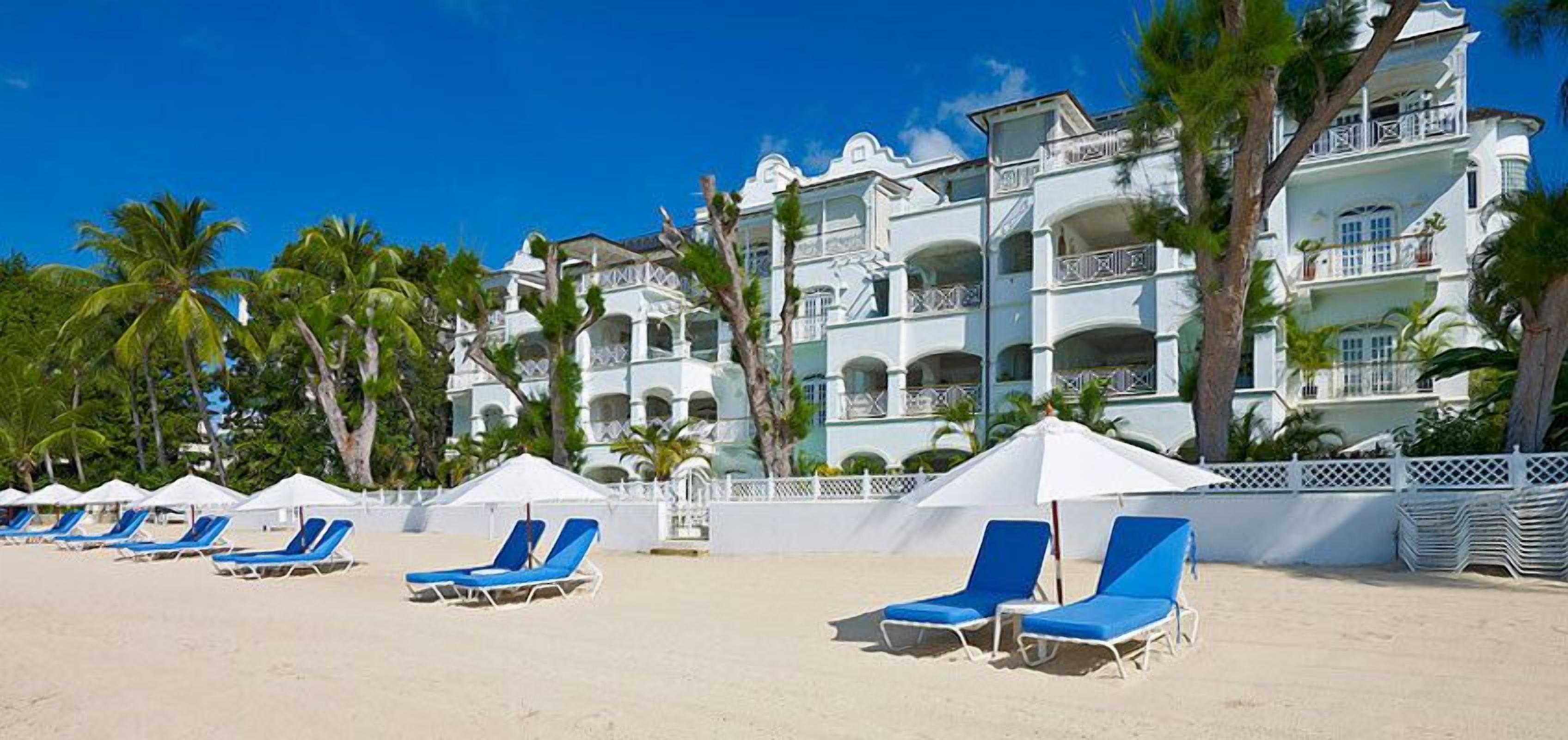 A beachfront hotel with multiple balconies, palm trees, and sun loungers.