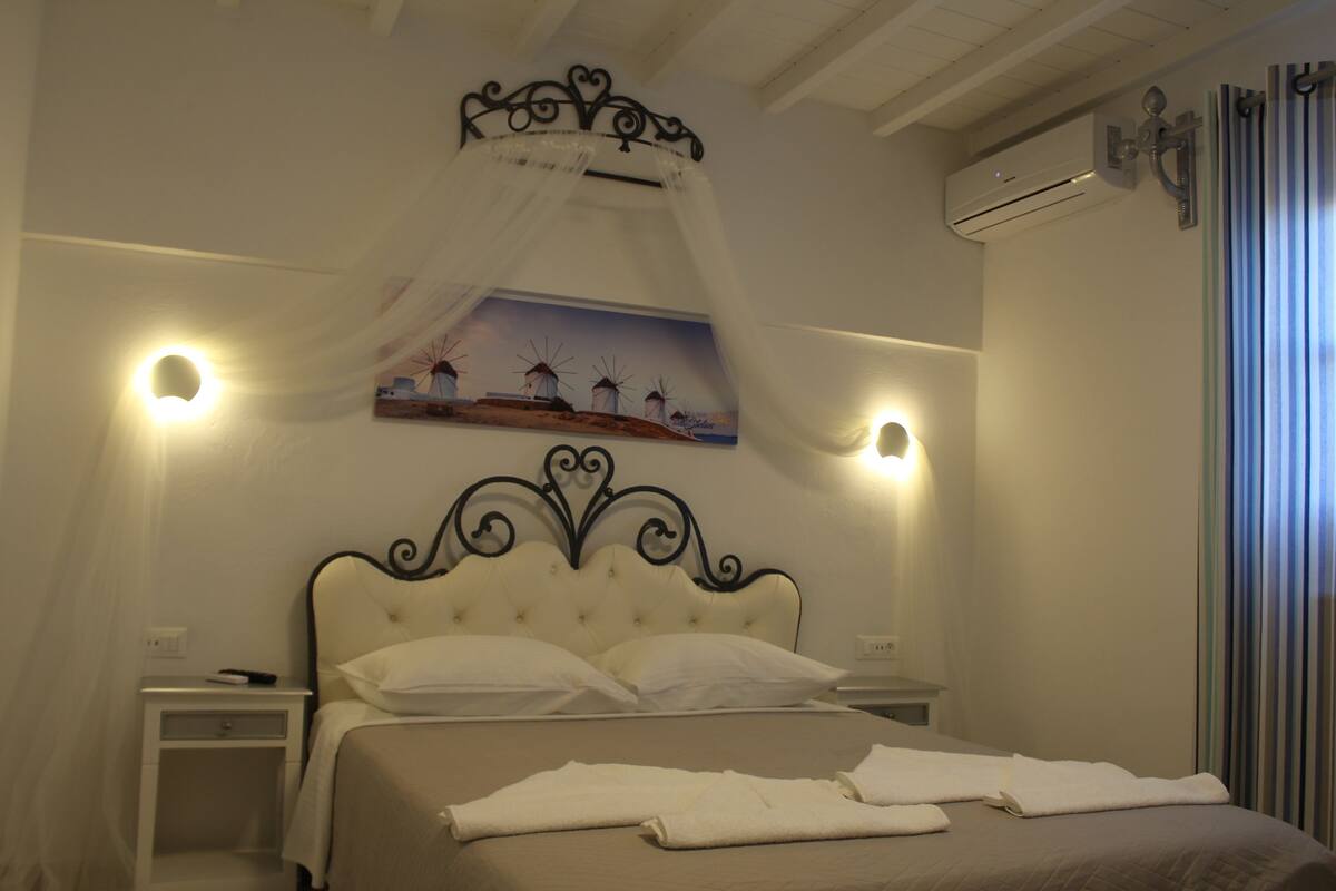 Una cama bien hecha con sábanas y almohadas blancas, un cabecero decorativo y un aire acondicionado de pared.