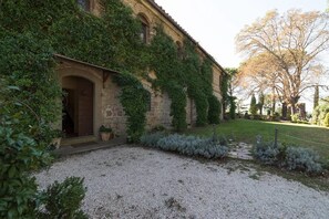 Un edificio histórico con fachada de piedra, ventanas en arco y un patio de grava.