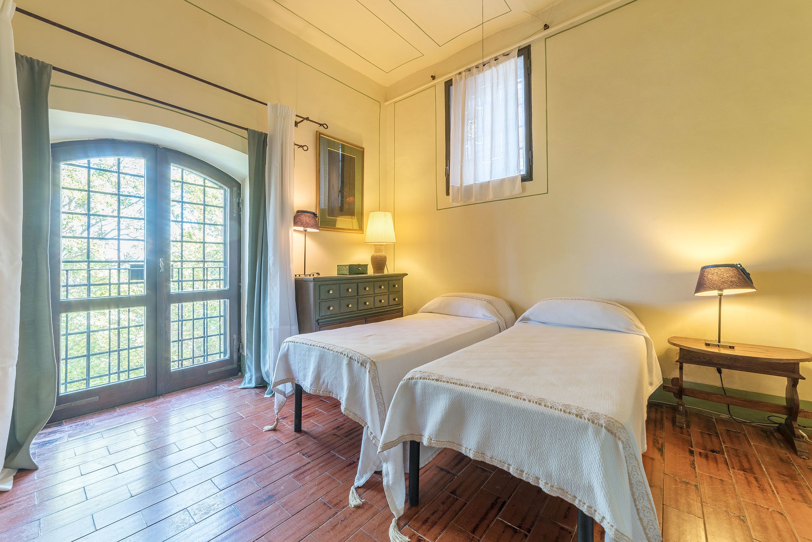 A room with two beds, a dresser, a lamp, and a window with curtains.