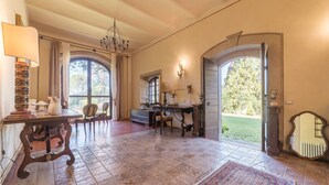 A spacious room with a large window, a chandelier, a desk, and a dining area. - Bomarzo Ancient Villa (Bomarzo)