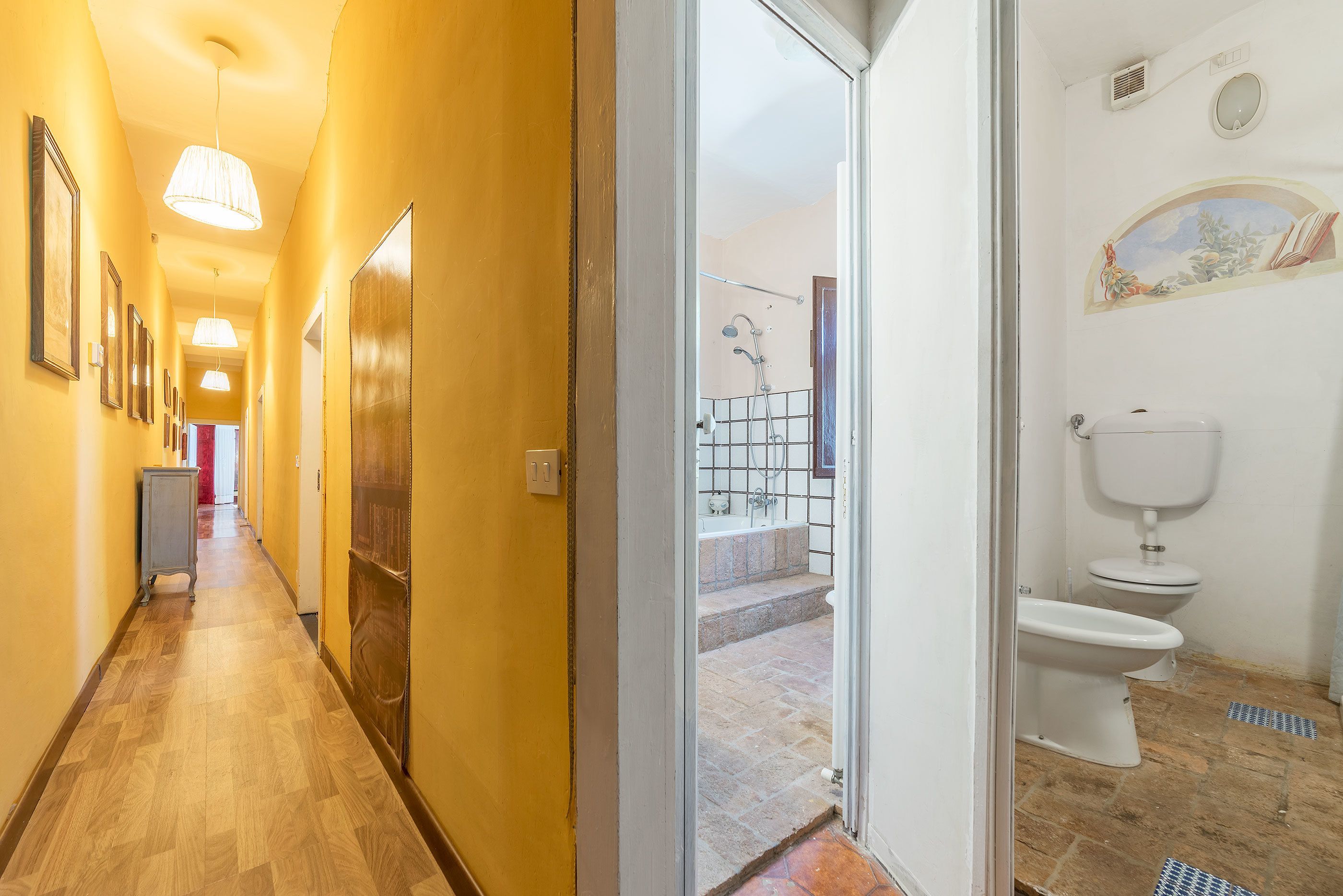 A hotel hallway with wooden flooring, a metal cart, and a door leading to a bathroom with a toilet and shower.