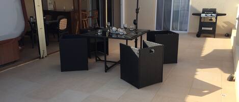 Une terrasse extérieure avec une table et des chaises, un barbecue et un espace abrité équipé d’un ventilateur et d’un distributeur d’eau.