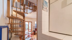 Una escalera con barandillas de madera que conduce a un piso superior, un área de comedor con una mesa y sillas, y una pizarra en la pared.