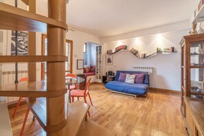 A modern living room with a glass table, orange chairs, a blue sofa, and a wooden staircase. - Boschetto Peaceful Apartment (Rome)