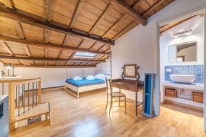 A bedroom with a wooden ceiling, a bed with blue bedding, a desk, and a bathroom with a blue-tiled sink. - Boschetto Peaceful Apartment (Rome)