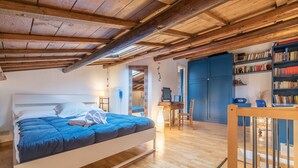 Un dormitorio con una cama, vigas de madera, un escritorio y una estantería.