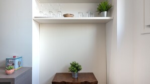 Une cuisine avec une table en bois, une étagère où sont rangés des verres et une plante en pot.