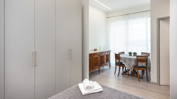 Une pièce comprenant un lit, une table à manger en bois avec des chaises, un buffet et une fenêtre avec des rideaux.