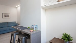 Une cuisine moderne avec un plan de travail gris, deux tabourets de bar, un canapé bleu et une petite plante en pot.