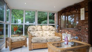 A spacious room with large windows, a wicker sofa set, a glass coffee table, and a brick wall. - Idylic country cottage with hot tub on private estate (Challock)