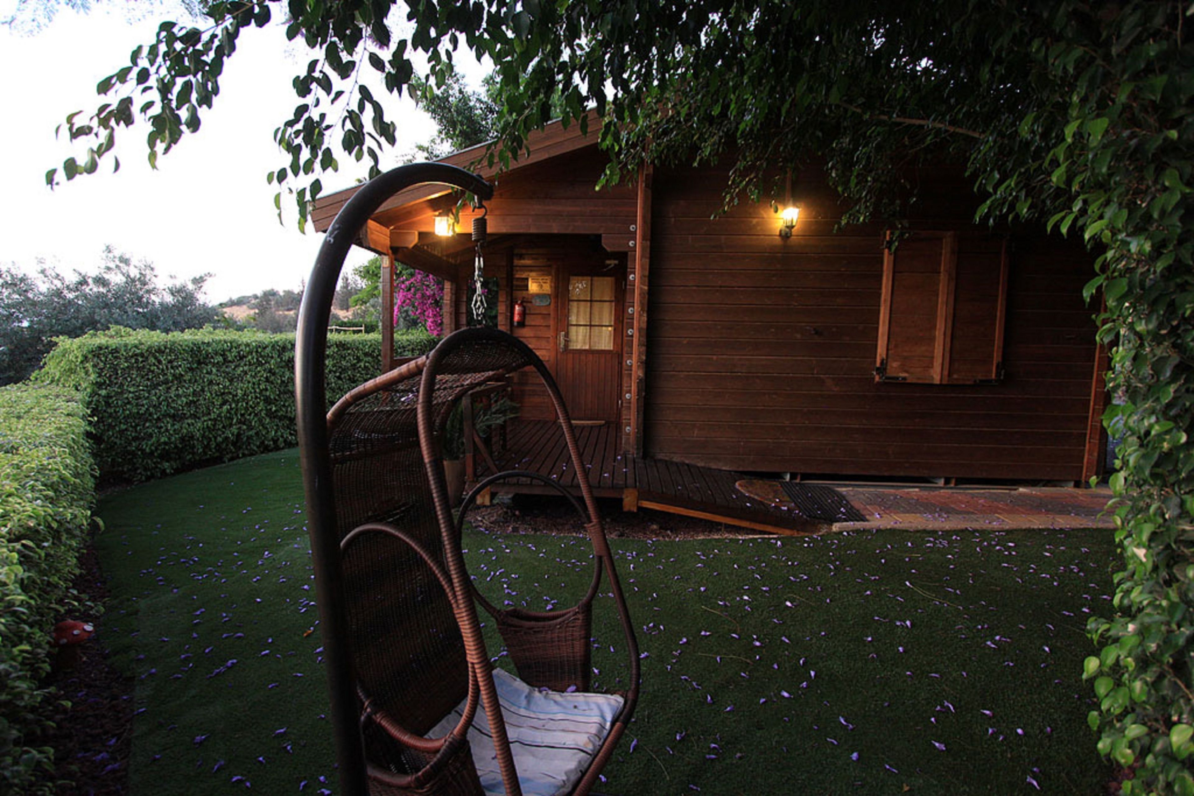 A wooden cabin with a swing chair in the garden.