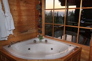 A wooden cabin with a large bathtub, wooden walls, and a window with a view of trees and mountains. - Eden Ramot Chalets (Ramot)