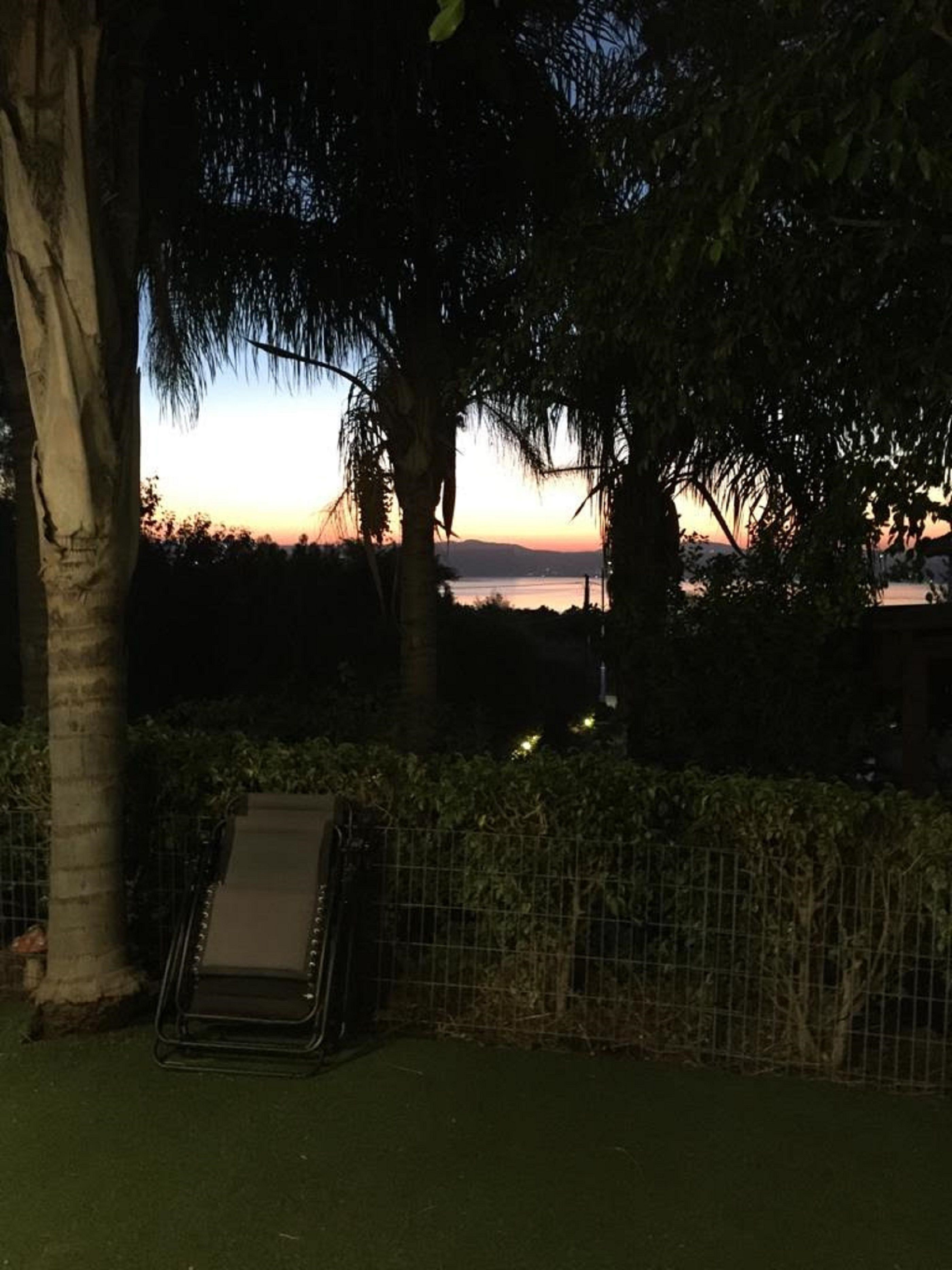 A hammock in a shaded area with a view of a sunset over water.