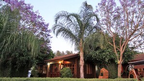A wooden house with a porch, surrounded by lush greenery and purple flowers. - Eden Ramot Chalets (Ramot)