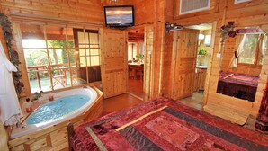 A wooden cabin with a large bedroom featuring a red quilt, a bathtub, and a television mounted on the wall. - Eden Ramot Chalets (Ramot)